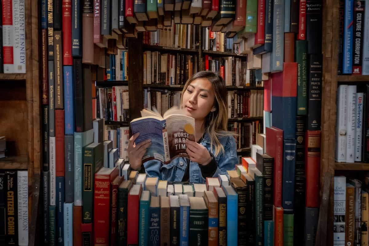 Grace reading through a circular opening framed by books at The Last Bookstore