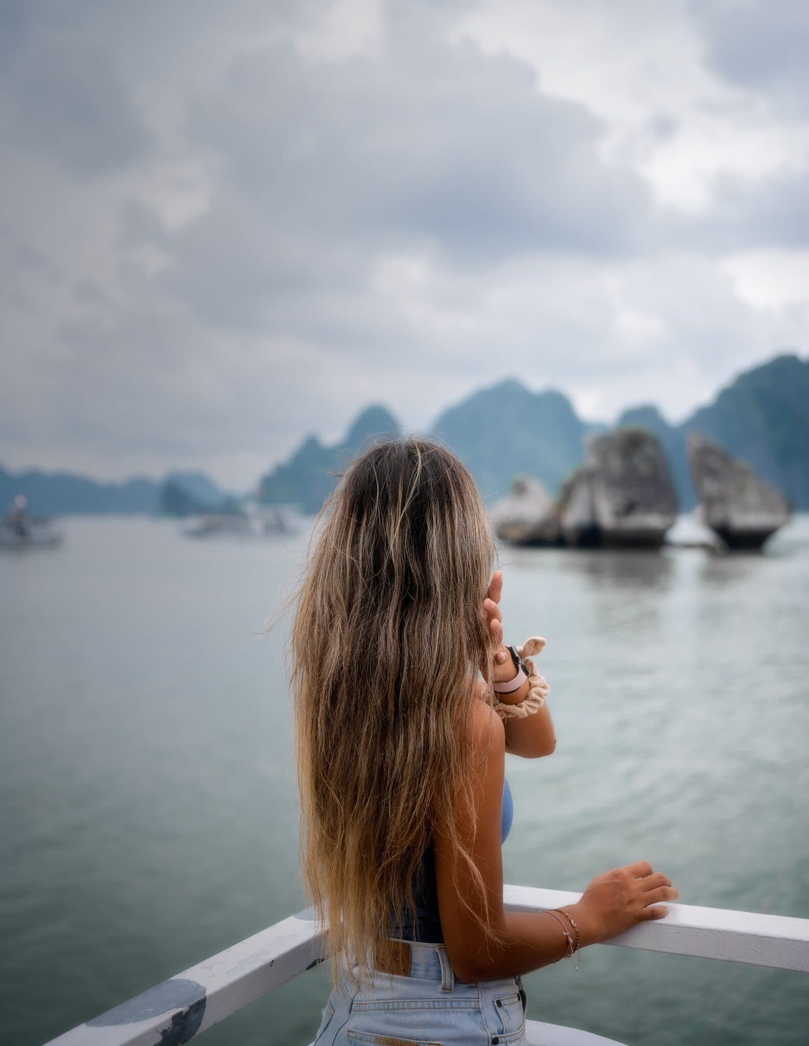 Grace standing on a boat deck in Ha Long Bay, Vietnam, surrounded by limestone islands