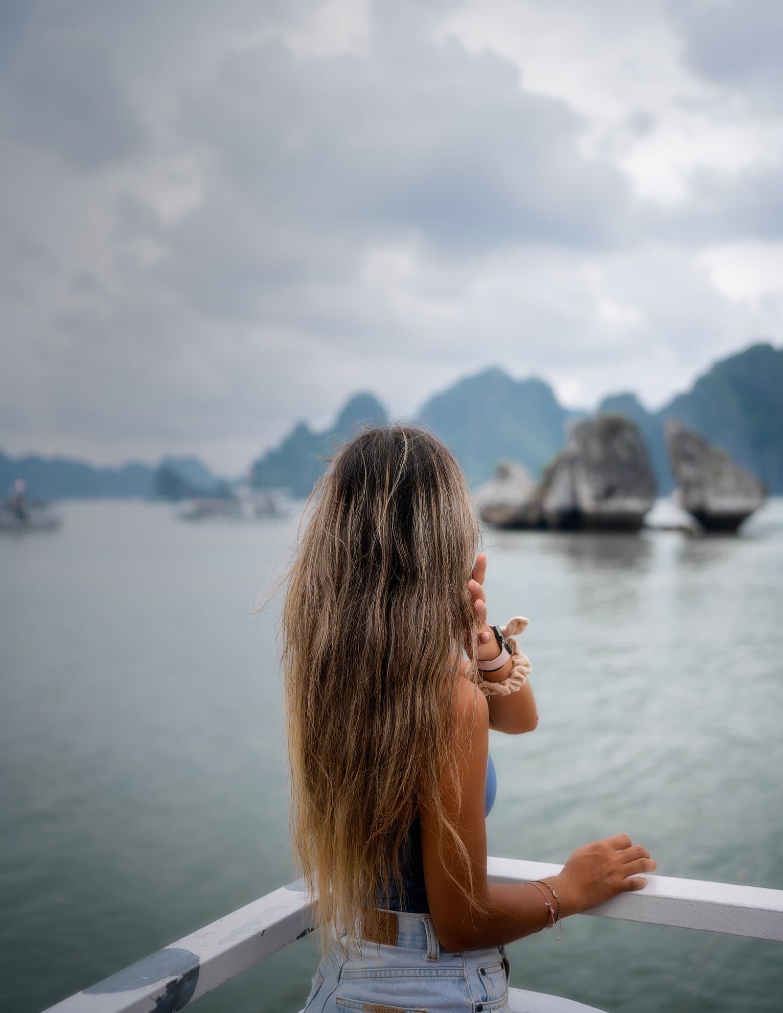 Grace standing on a boat deck in Ha Long Bay, Vietnam, surrounded by limestone islands