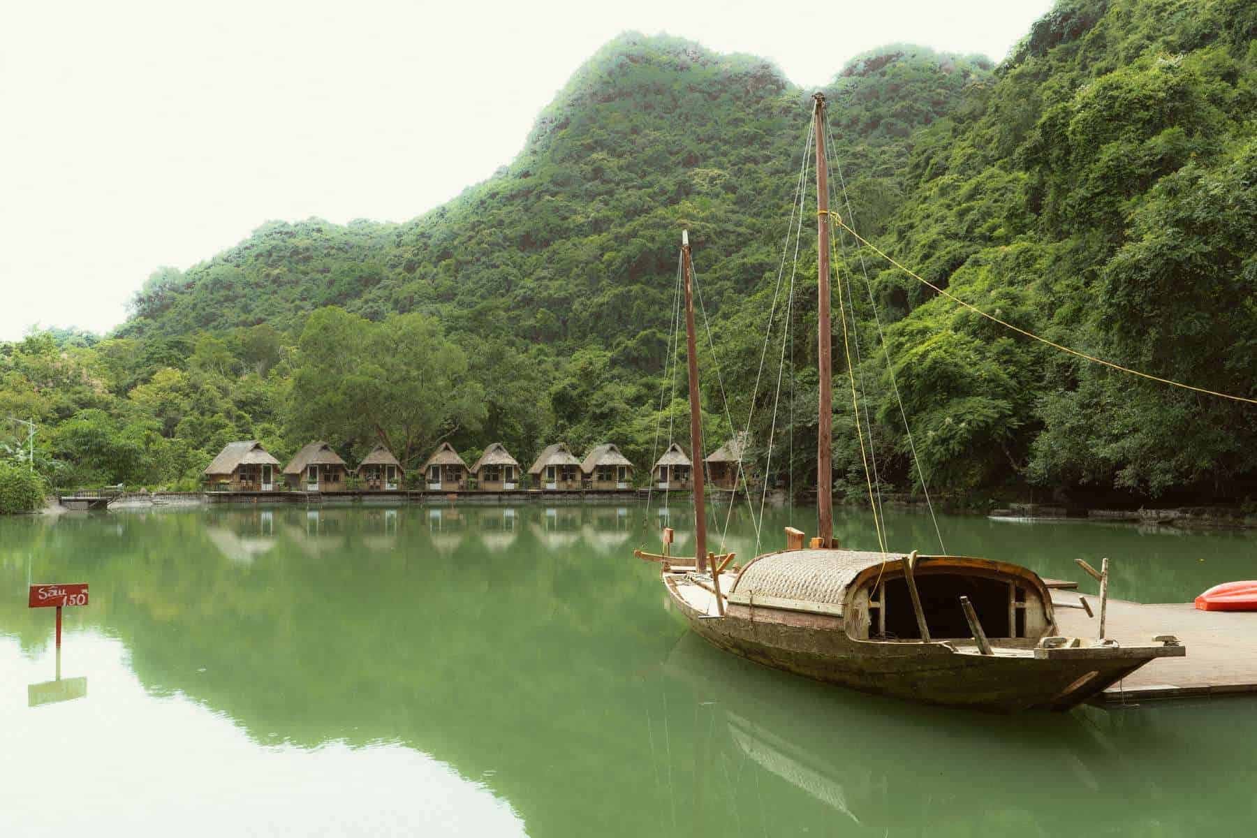 Wooden boat on green water below forested cliffs on Cat Ba Island