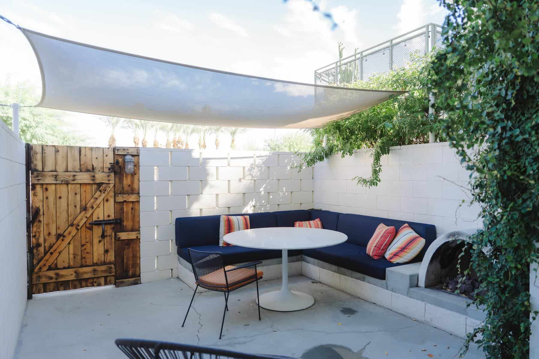 Our walled patio at Ace Hotel Palm Springs, with a navy cushioned bench, round table, fire pit, shade sail and wooden gate